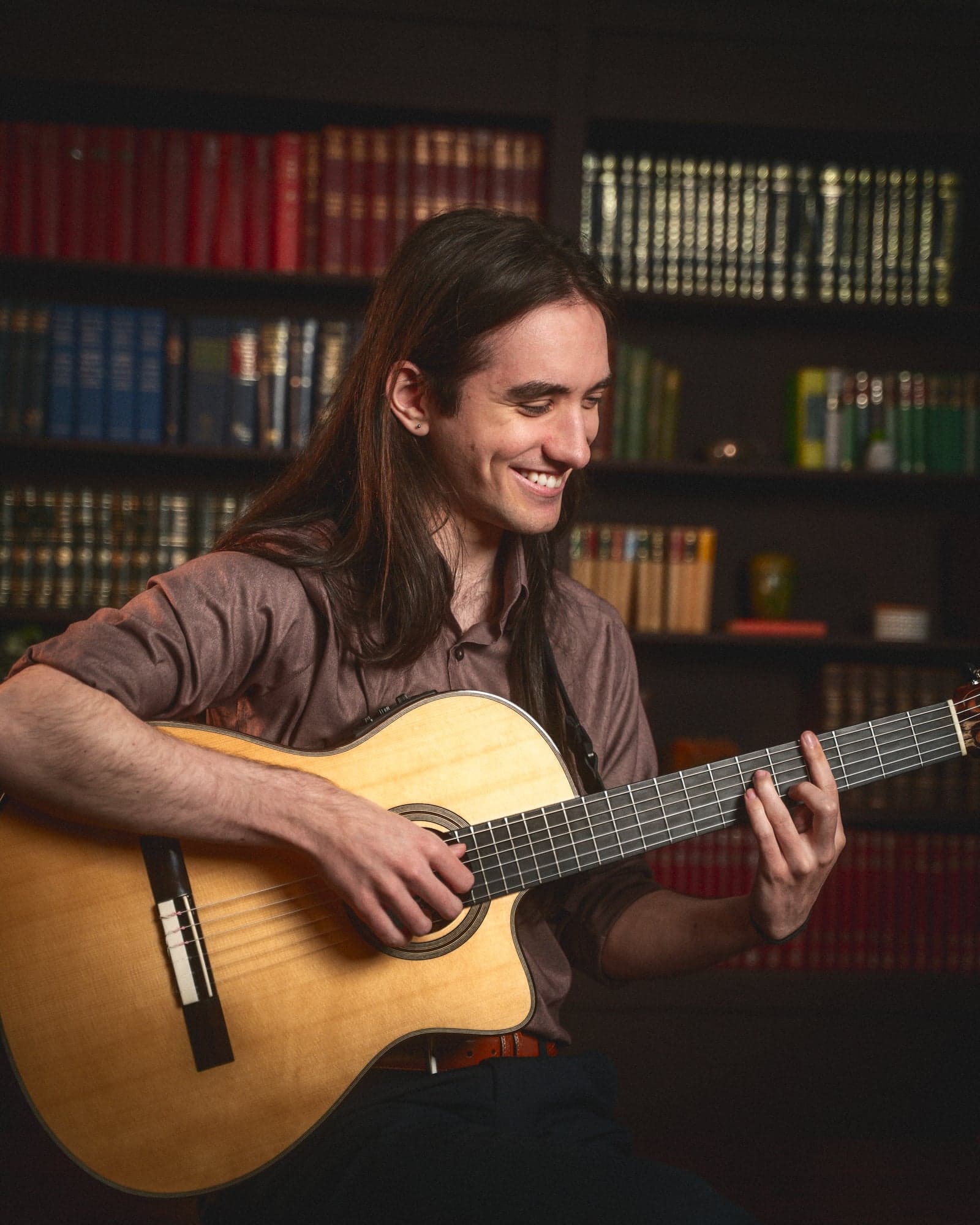 Sam smiling with guitar, bookshelf